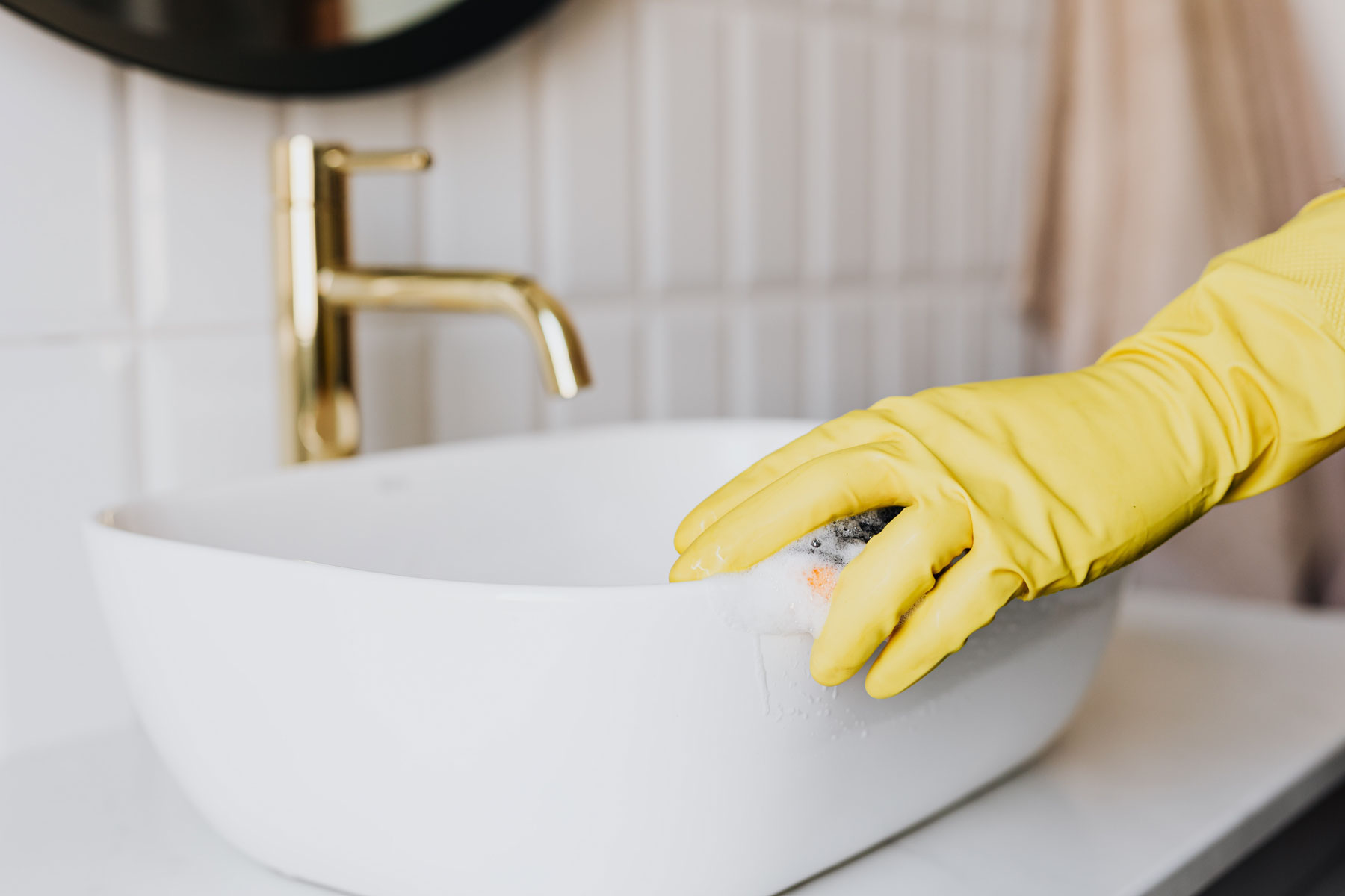 Cleaning bathroom sink with yellow gloves.